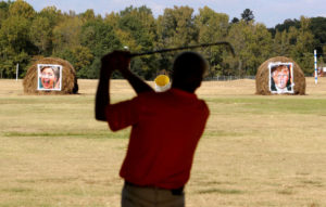 Mike Williams, owner of the Alpine Target Golf Center, shows off his swing at a driving range with hay bales covered with the portraits of U.S. presidential nominees Hillary Clinton and Donald Trump, which are used as a mock polling station, at Alpine Target Golf Center in Longview, Texas November 2, 2016. REUTERS/Todd Yates